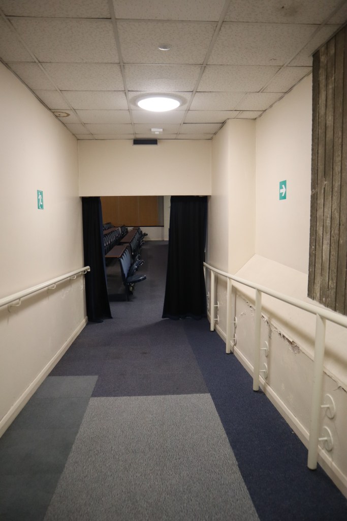 The view of the ramp. It is a blue, low pile carpet with curtains at the end.