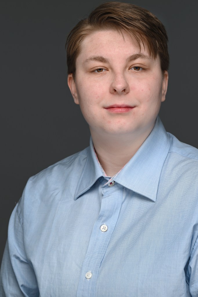Eli, a white androgynous person with brown hair in a blue shirt.