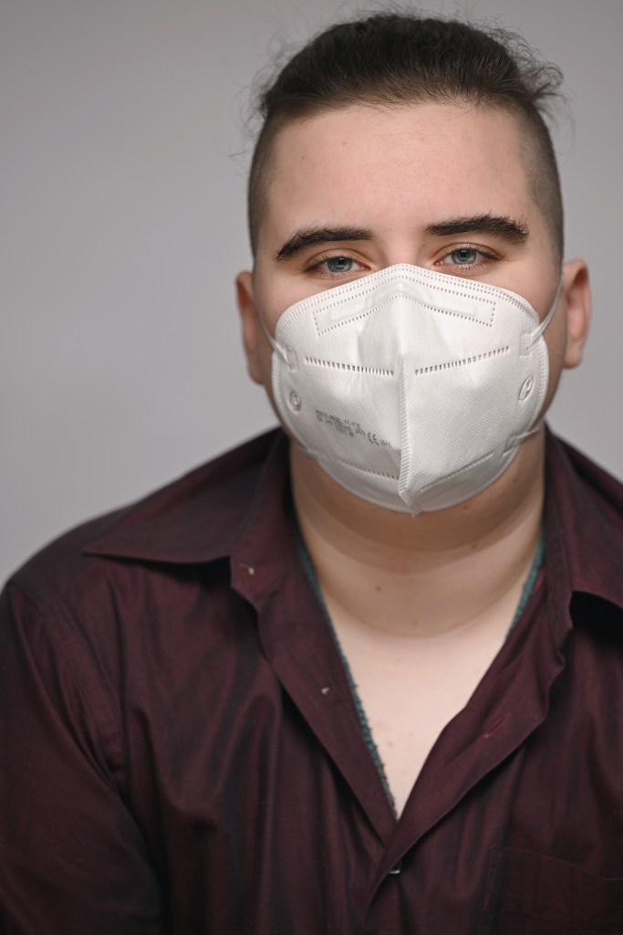 Aspen, a white masc person, in a dark red shirt and a white face mask.